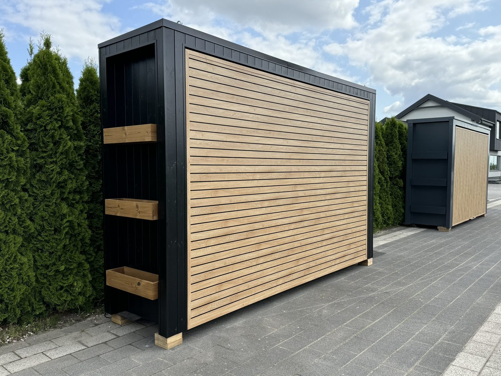 Enclosed outdoor kitchen with a black casing, wooden slat detailing and side shelves.