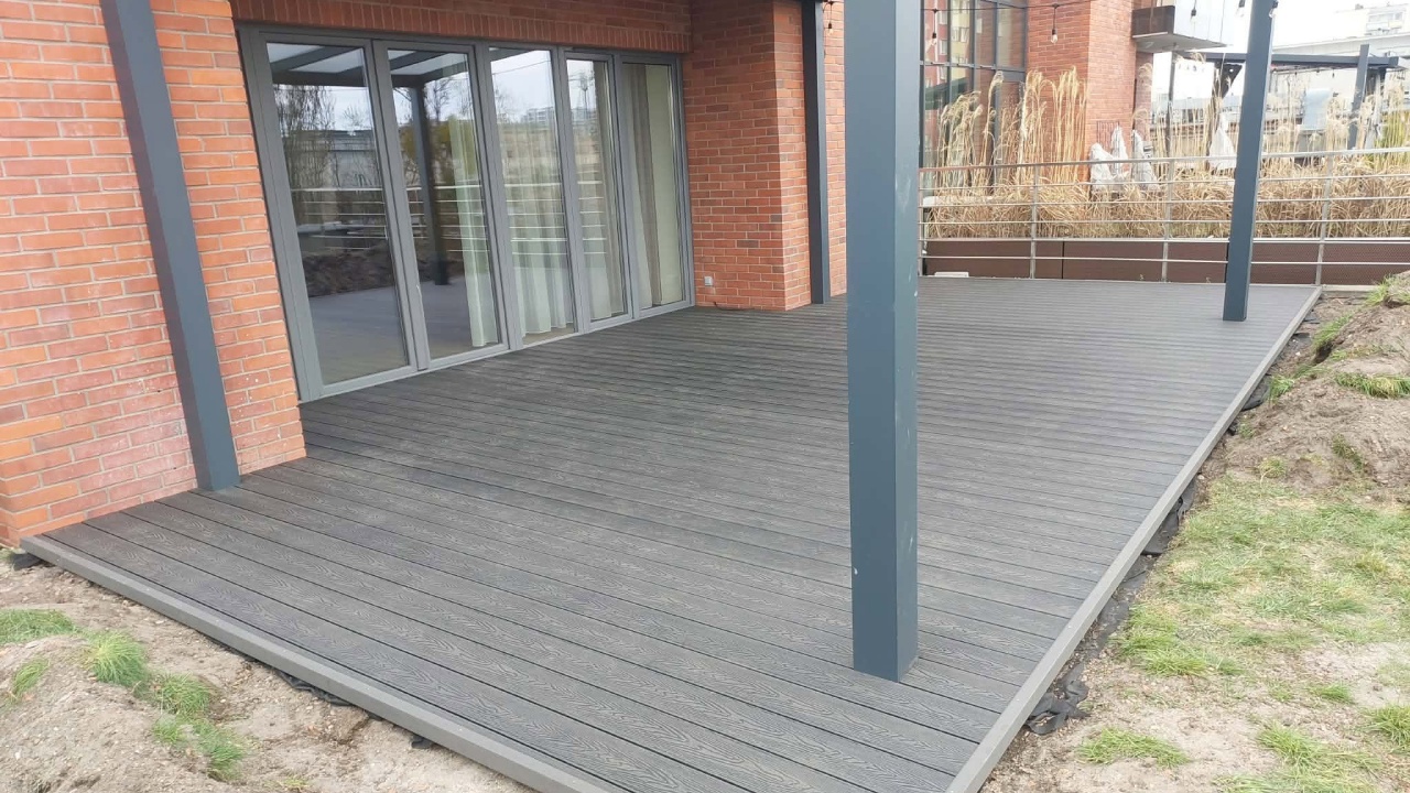 A terrace made from graphite-grey composite decking boards beside a red-brick building with large glazed windows.