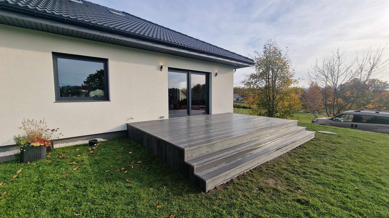 A terrace made from light grey composite decking boards, with steps leading down to the lawn beside a white house.
