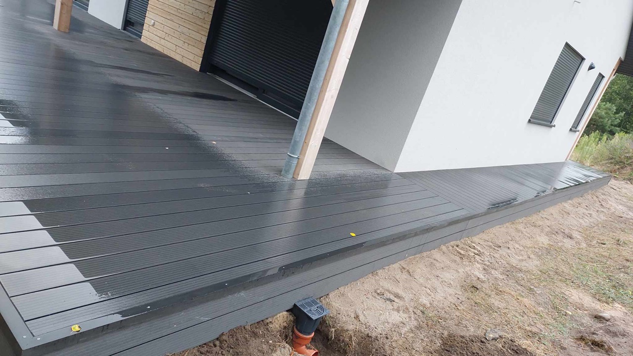 Modern dark grey composite decking terrace installed beside the white façade of a house.