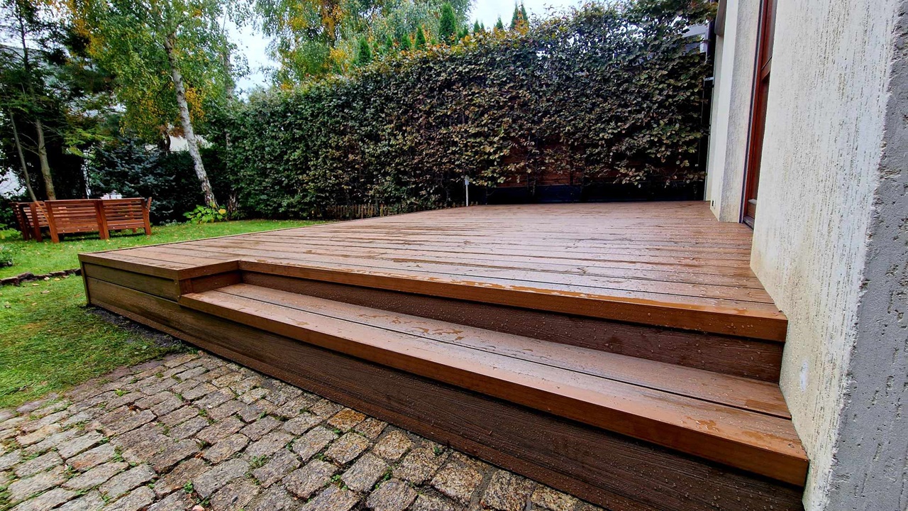 Brown composite terrace with steps beside a building, situated next to a garden and paved area.