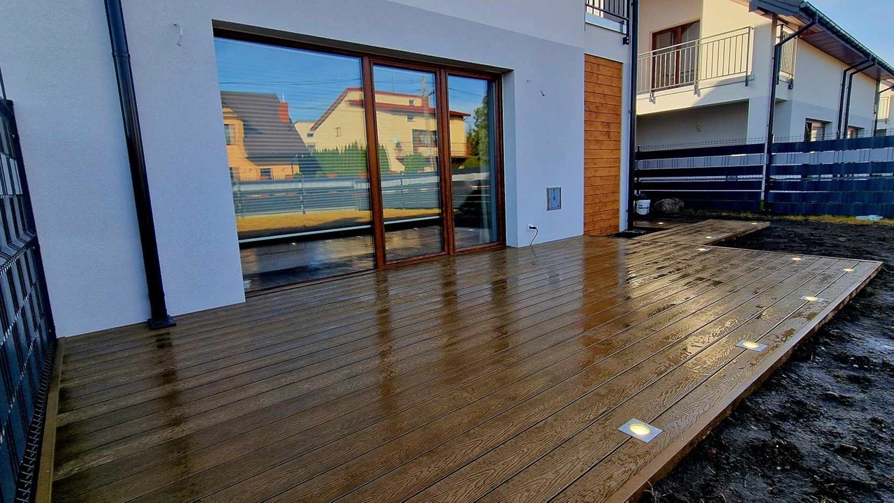 Brown composite decking board terrace with built-in spotlights beside a house with large patio doors.