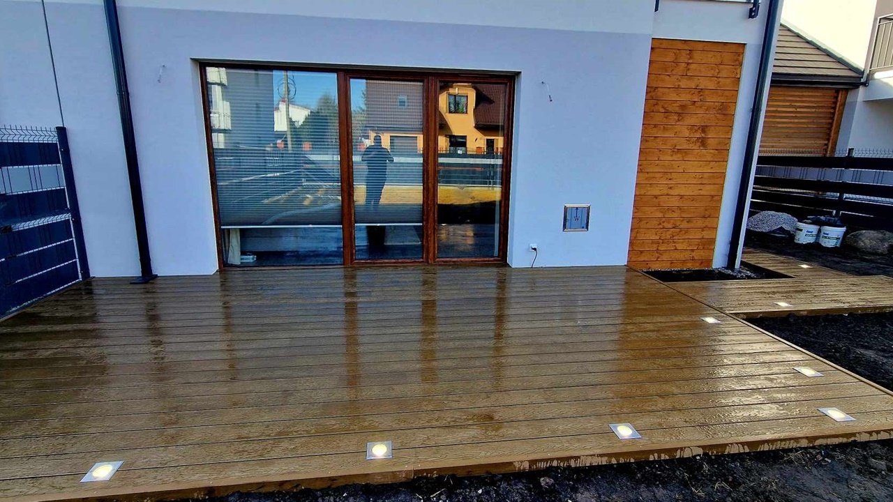A light brown composite deck with built-in LED lighting beside large glazed patio doors.