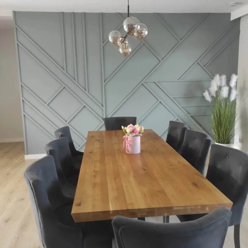 A grey wall decorated with a geometric pattern of DIY strips in a dining room with a wooden table and chairs.