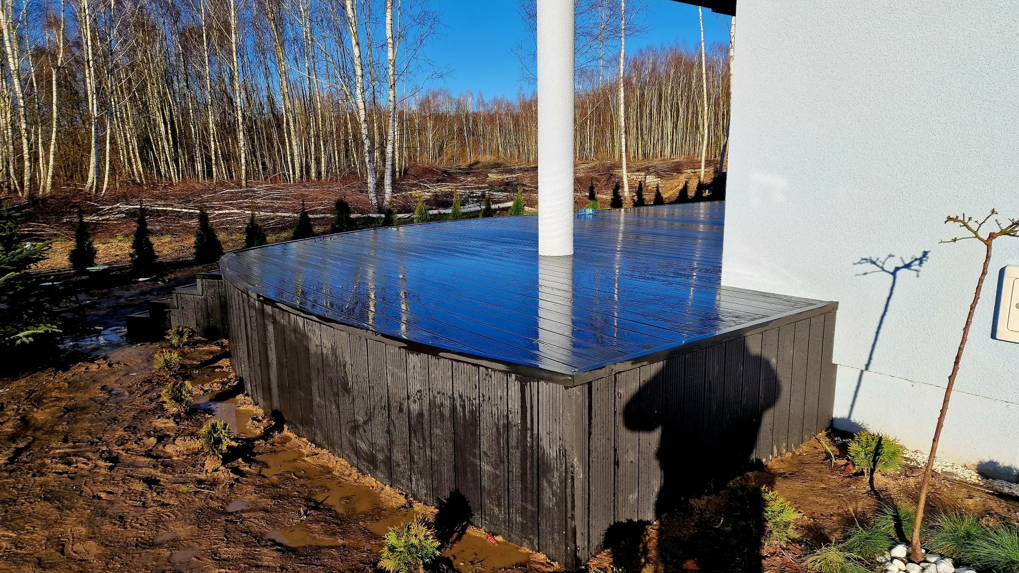 Dark composite decking terrace with vertical edge cladding beside a modern house against a woodland backdrop.