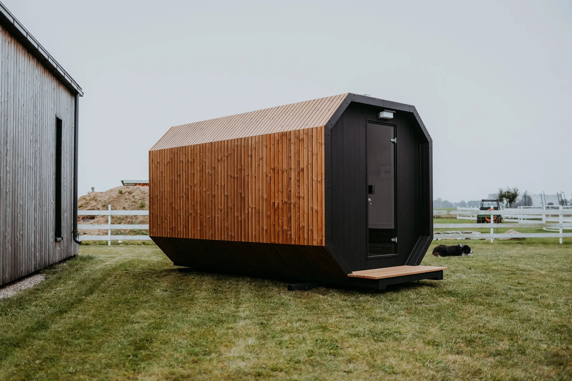 A modern, freestanding garden sauna finished with wooden slats, standing on a lawn.
