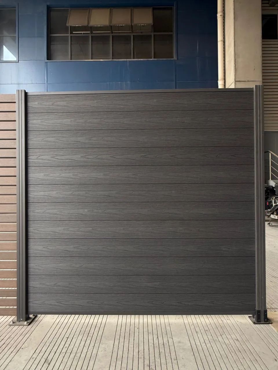 Dark grey composite fence panel with a wood texture installed on vertical posts.